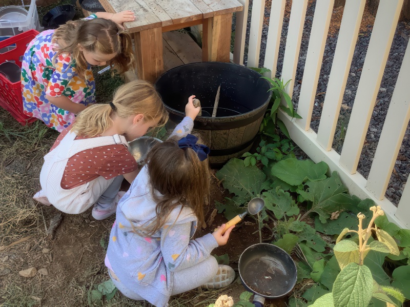 Three children engaged in playful activities in the dirt, utilizing pots as tools for their creative outdoor exploration.