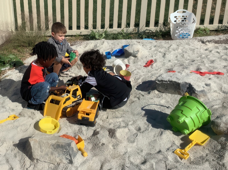 Three children engaged in play within a sandbox, using various toys to build and explore their creative ideas.